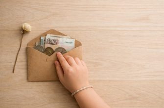 Язык денег, на котором мы молчим с детьми 6 Детская рука закрывает крафтовый конверт с рублевыми купюрами и монетами — метафора детского отношения к деньгам и финансовых установок.